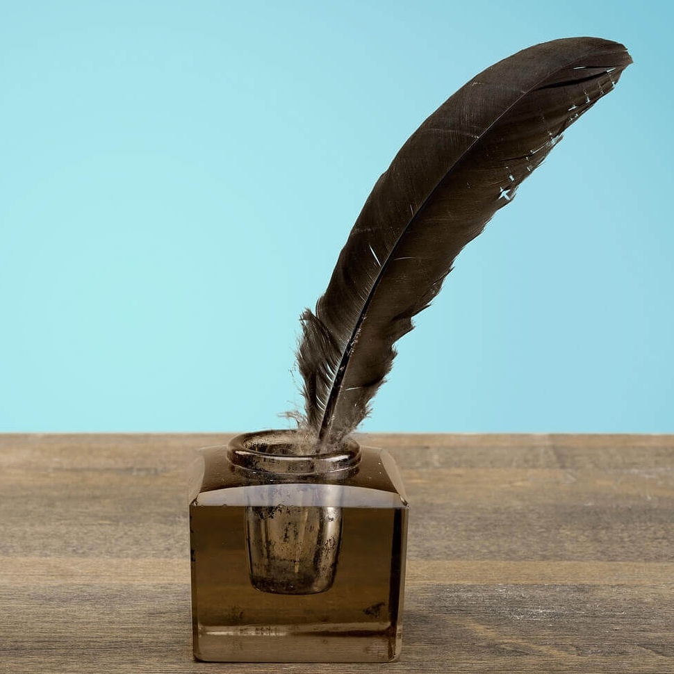 quill in ink jar on a wooden surface with clear blue sky in the background